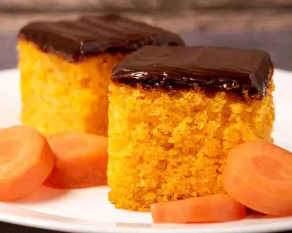 Due fette di ciasto marchewkowe, soffice e arancione, ricoperte di glassa al cioccolato fondente, con fettine di carota fresca intorno.
