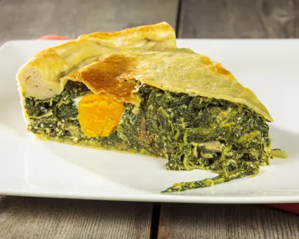 Una fetta di torta di bietole e ricotta senza sfoglia, con un uovo intero al centro, su un piatto bianco.