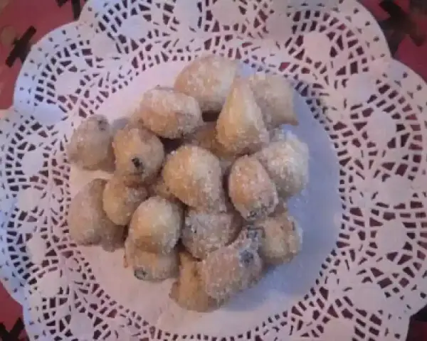 Un mucchietto di castagnole montersino, dolcetti dorati e zuccherati, adagiati su un centrino di pizzo bianco.