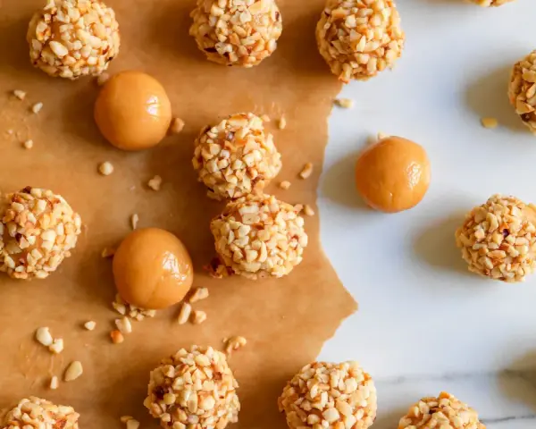 Piccoli bomboloni caramelle ricoperti di noccioline tritate, alcuni con un ripieno di caramello visibile.