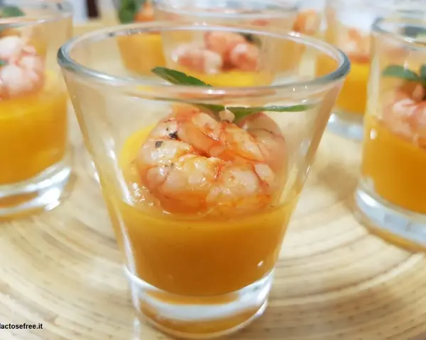 Deliziosi gamberi aperitivo in bicchierini con crema arancione e foglioline verdi.