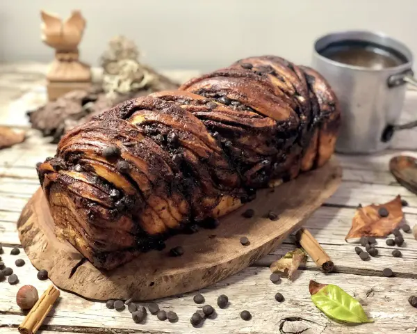 Babka ponczowa, intrecciata e ricca di gocce di cioccolato, pronta per essere gustata con una tazza di caffè.