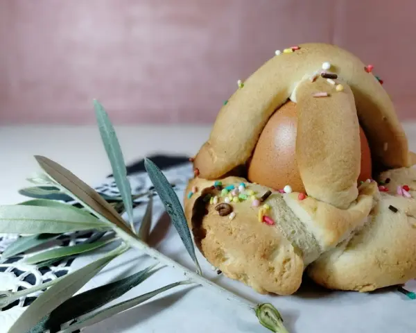Dolci biscotti con uovo sodo, decorati con zuccherini colorati, pronti per essere gustati. Un ramoscello d'ulivo completa la scena.