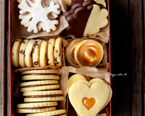 Scatola piena di deliziosi ciasteczka maślane: a fiocco di neve, al cioccolato, con ripieno di caramello e a forma di cuore.