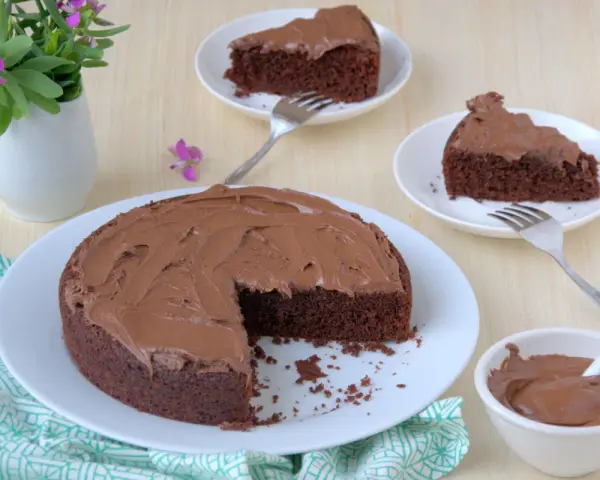 Deliziosa torta al cioccolato senza glutine con fecola di patate, ricoperta di glassa al cioccolato, servita su piatti bianchi con forchette.