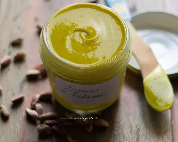 Un vasetto di cremosa crema di pistacchio, con pistacchi sparsi intorno. Perfetta per dolci e colazioni.