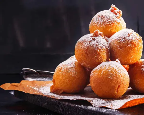 Pile di frittelle di mele e uvetta con lievito di birra, spolverate di zucchero a velo, su carta da forno.