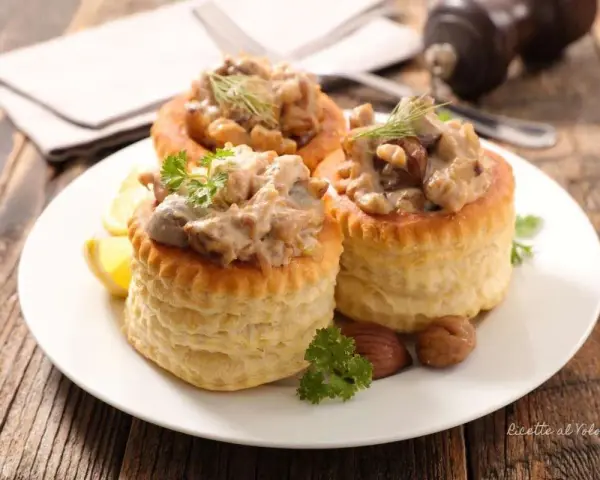 Tre vol-au-vent con funghi cremosi, guarniti con prezzemolo e aneto, su un piatto bianco con spicchi di limone.