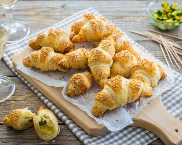 Croissant dorati con ripieno di pasta sfoglia e semi di sesamo, pronti per essere gustati con un bicchiere di vino.
