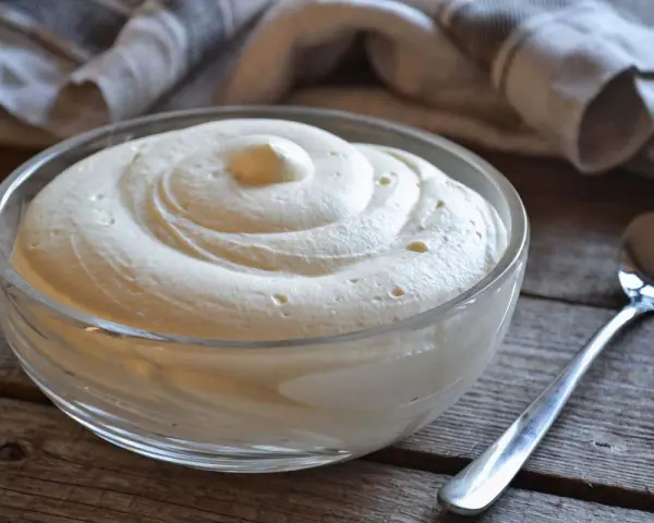 Una ciotola di soffice crema al mascarpone senza lattosio, pronta per essere gustata. Un cucchiaino argentato attende accanto.