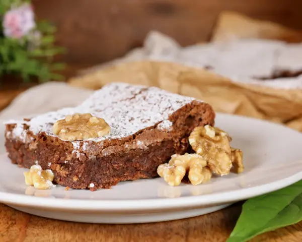 Una fetta di torta noci e cioccolato senza farina, cosparsa di zucchero a velo e decorata con noci intere.