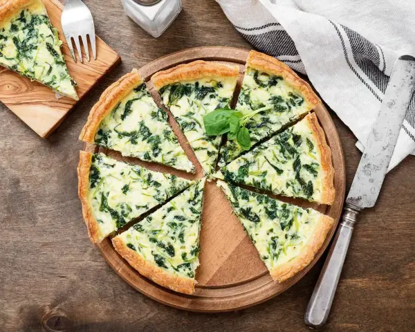 Torta salata spinaci e mozzarella, con un tocco di speck affumicato, tagliata a spicchi su un tagliere di legno.