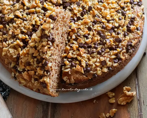Torta noci e amaretti, soffice e golosa, ricoperta di noci tritate e gocce di cioccolato.