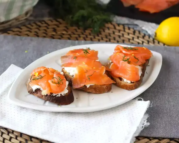 Tre bruschette con salmone affumicato, formaggio cremoso e aneto, guarnite con scorza di limone.
