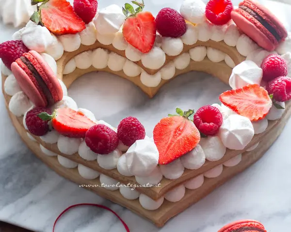 Cream tart numero 1 a forma di cuore, decorata con panna, fragole, lamponi e macarons.