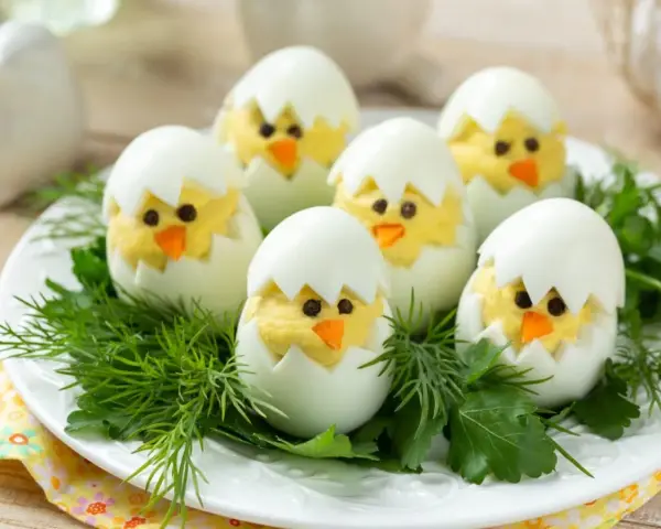 Uova sode ripiene a forma di pulcino, un'idea divertente per le jajka faszerowane pasquali, adagiate su un letto di erbe aromatiche.
