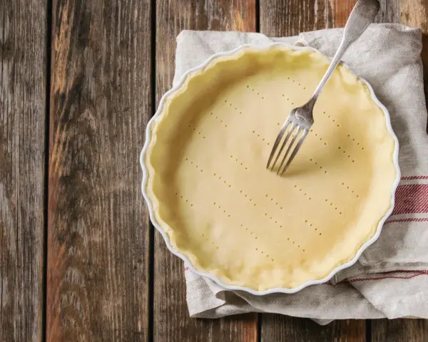 Pasta frolla salata con olio e parmigiano pronta per essere infornata. Una forchetta è appoggiata sulla base bucherellata.