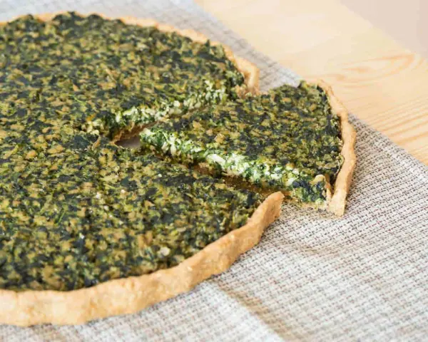 Una fetta di torta salata vegana spinaci, con una crosta dorata e un ripieno verde e cremoso, pronta per essere gustata.