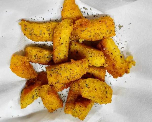 Croccanti bastoncini di polenta taragna fritta, dorati e conditi con erbe aromatiche, adagiati su carta bianca.