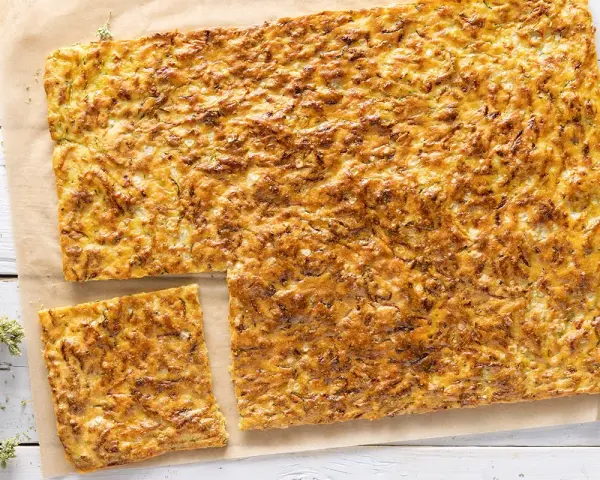 Schiacciata di zucchine e cipolle dorata e croccante, tagliata a pezzi su carta da forno.