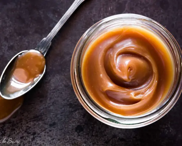 Un cucchiaio pieno di crema pasticcera al caramello salato, accanto a un barattolo dello stesso delizioso composto.