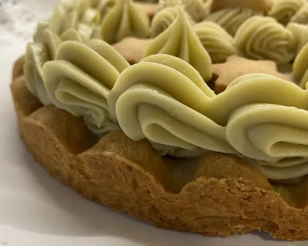 Torta con bordi croccanti e un abbondante strato di ganache pistacchio, decorata con biscotti a forma di stella.