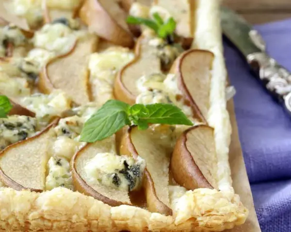 Deliziosa pizza zola e pere su pasta sfoglia croccante, guarnita con foglie di menta fresca. Un connubio di sapori unico.
