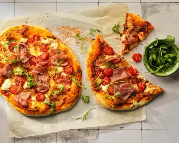 Pizza con mascarpone, pomodorini, prosciutto crudo e rucola, su carta forno.