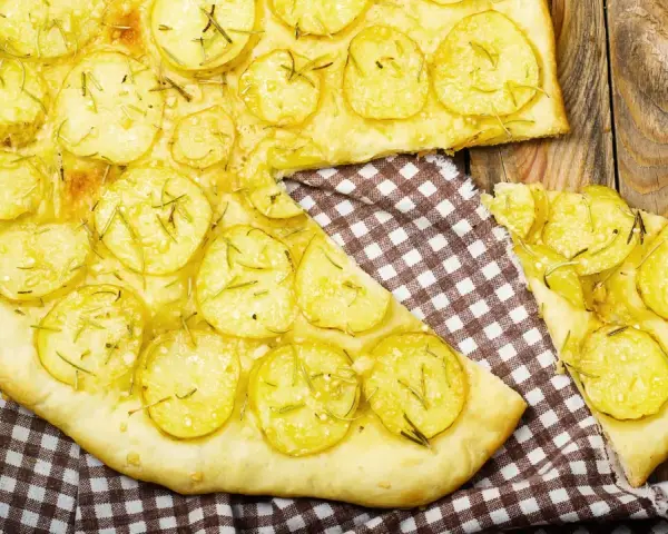 Schiacciata di patate con farina di ceci, guarnita con rosmarino fresco, su un tagliere di legno rustico.