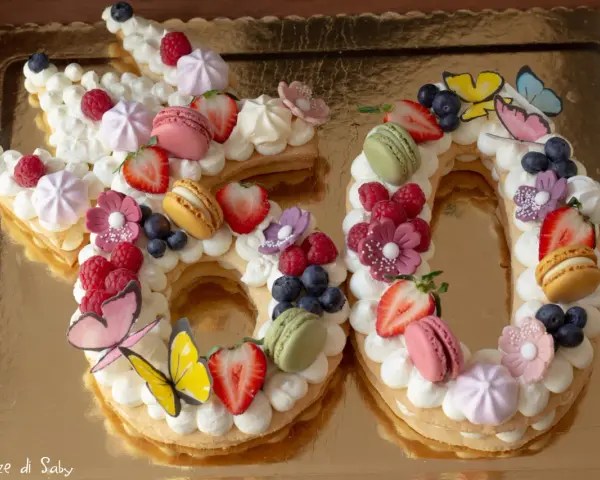 Una torta numero 60 decorata con panna, frutta fresca, macarons e farfalle. Una deliziosa ricetta torta numero per festeggiare.