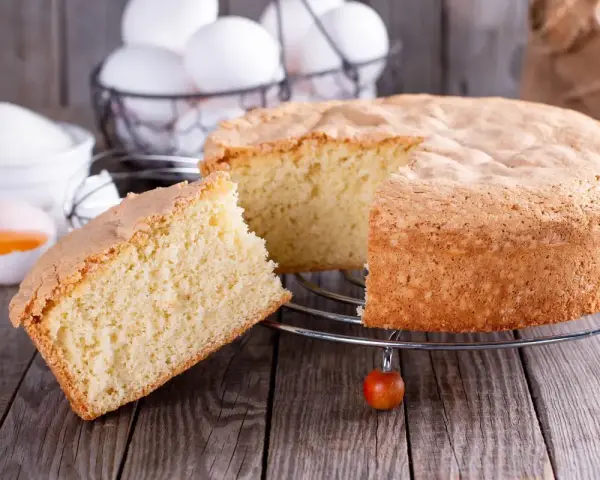 Un soffice ciasto drozdzowe, appena sfornato, con una fetta tagliata. Ingredienti per la torta lievitata sono visibili sullo sfondo.