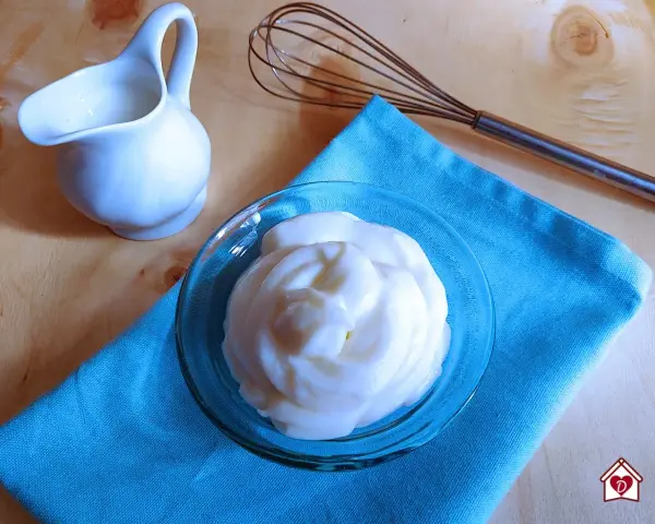 Crema soffice e vellutata, una delizia preparata con yogurt greco. Accanto, una piccola brocca e una frusta, pronti per creare altre bontà.