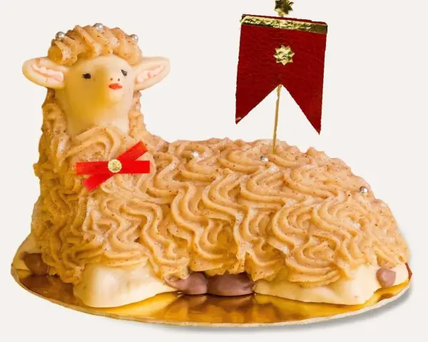 A decorative cake shaped like a lamb, with piped frosting and a red ribbon.