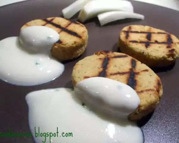 Deliziosi medaglioni di ceci grigliati, serviti con una salsa bianca cremosa e guarniti con erbe aromatiche.