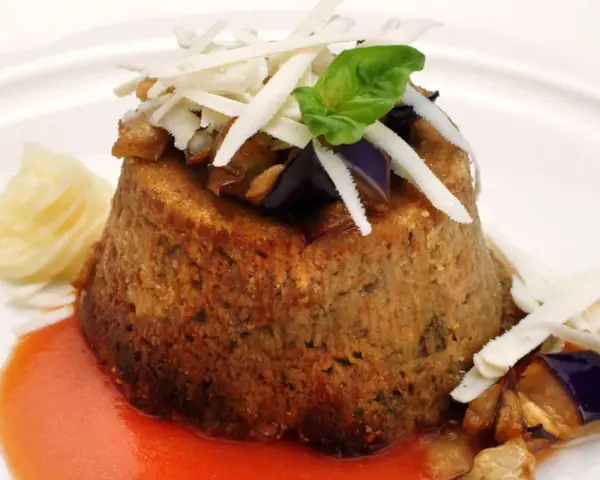 Sformato di melanzane leggero, guarnito con scaglie di formaggio, basilico e servito con salsa rossa e purè.