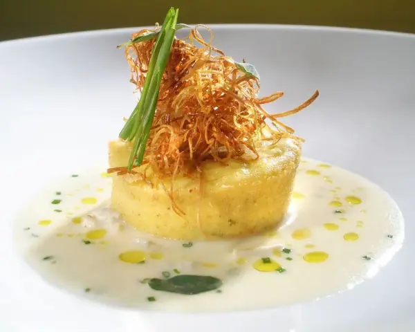 Flan di porri con salsa di acciughe, guarnito con cipolla croccante e erbe aromatiche. Un piatto raffinato che celebra i sapori del mare e della terra.