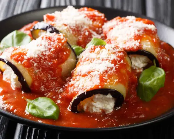 Involtini di melanzane vegetariani ripieni di ricotta, coperti da sugo di pomodoro e parmigiano, guarniti con basilico fresco.