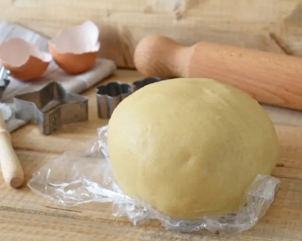 Impasto per kruche ciasto, stampini per biscotti, gusci d'uovo e mattarello pronti per preparare dolci deliziosi.