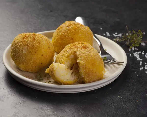 Tre arancini dorati su un piatto, uno aperto rivela il ripieno di riso. Un invito a provare il nostro arancini ricetta.