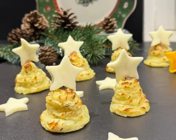 Alberelli di patate decorati con stelle di formaggio, su un piatto natalizio con pigne e rami di abete.
