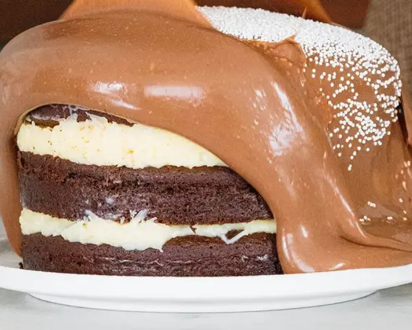Torta al cioccolato a strati con glassa al cioccolato fusa che cola, decorata con perline bianche. Un vero tsunami di dolcezza!