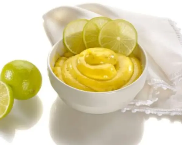 Una ciotola di cremosa crema al lime, guarnita con fette di lime fresco e accompagnata da lime interi e a metà.