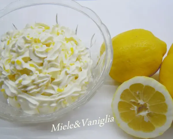 Una ciotola di panna montata con scorza di limone, accanto a limoni freschi. Perfetta per una ganache al limone leggera e profumata.