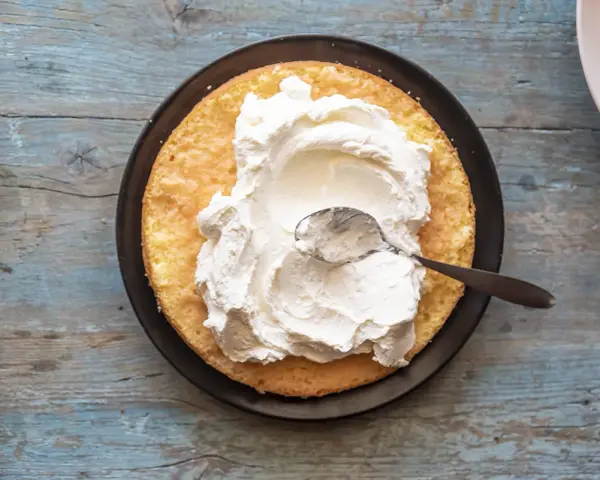 Una fetta di pan di spagna attende la sua deliziosa crema allo yogurt, spalmata con un cucchiaino.