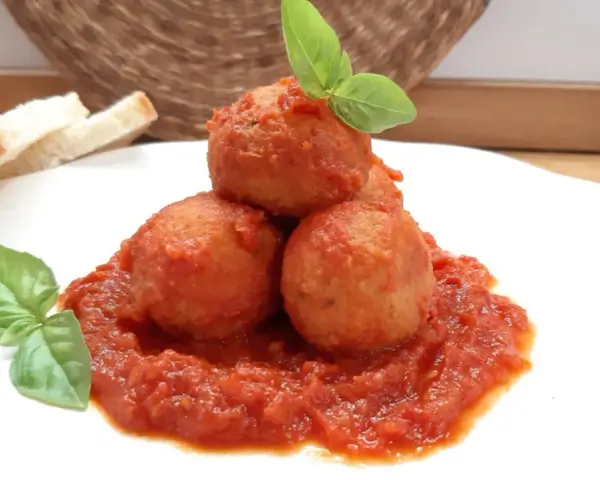 Polpette di pane in umido, un piatto confortante con pomodoro e basilico, accompagnato da fette di pane.