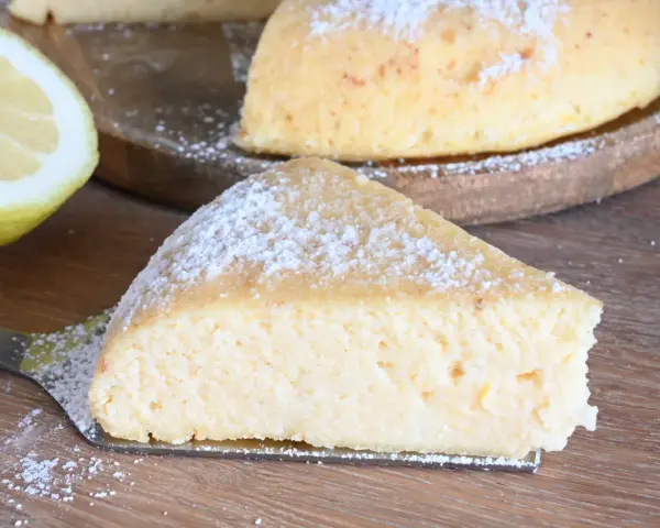 Una fetta di torta con semola, spolverata di zucchero a velo, accanto a un limone fresco.