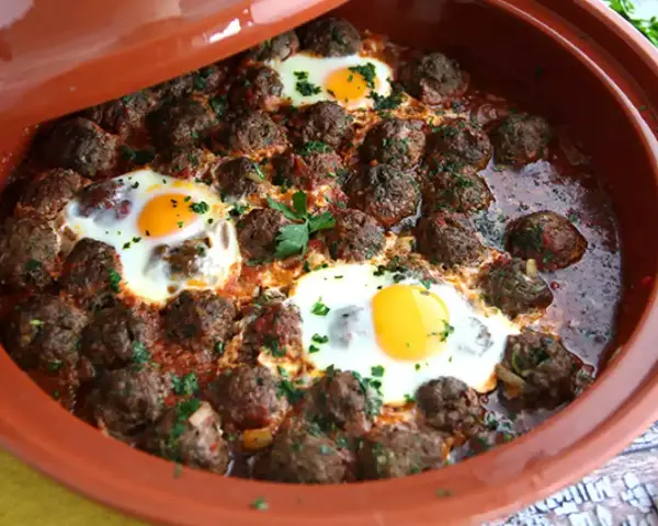 Polpette marocchine in umido con uova cotte nel tajine, guarnite con prezzemolo fresco.
