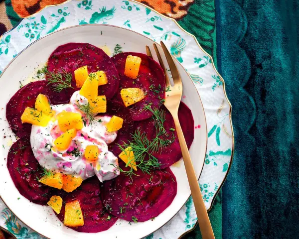 Delizioso carpaccio di barbabietola con crema, arancia e aneto su un piatto decorato.