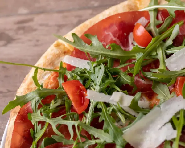 Pizza bresaola rucola e grana: un tripudio di sapori con bresaola, pomodorini, rucola fresca e scaglie di grana.