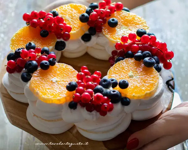 Delizioso tort pavlova a forma di corona, decorato con fette d'arancia, ribes rosso e mirtilli.